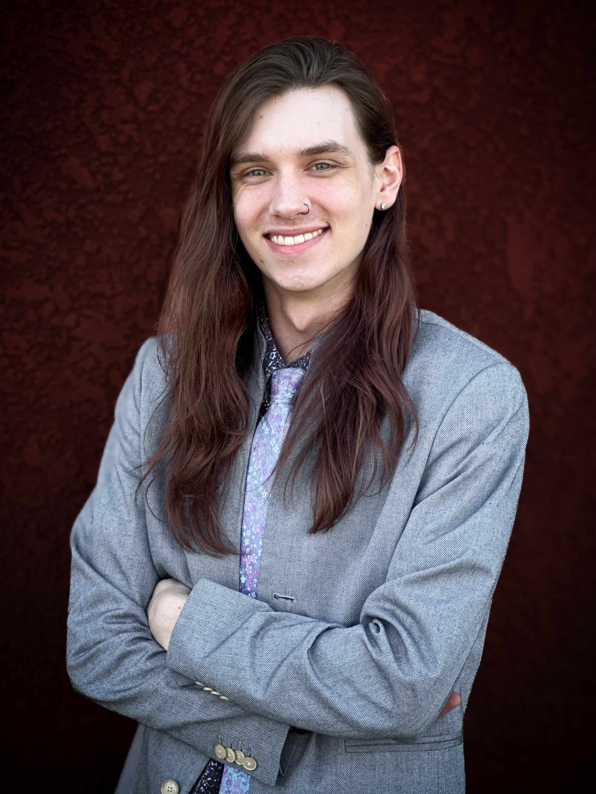 Photo of Lane. He has long hair and is against a red wall.